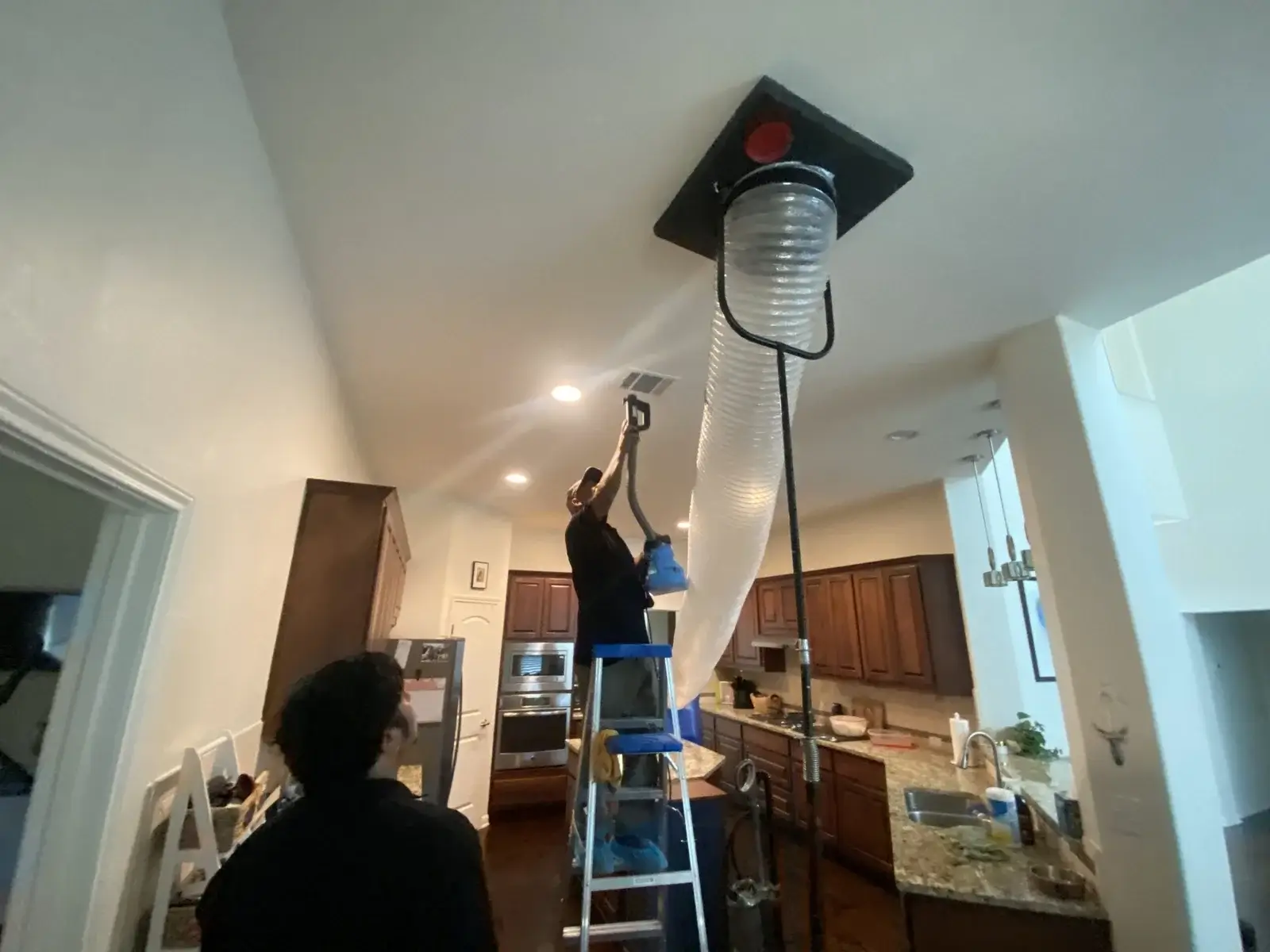 Negative air machine attached to the ceiling while our technician is cleaning the air duct using vacuums machine